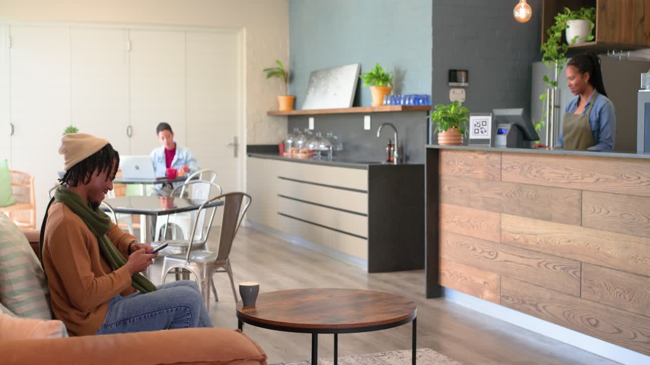 Uomo afroamericano che prende una tazza da un barista, si dirige verso il divano per controllare lo smartphone, spazio per la copia