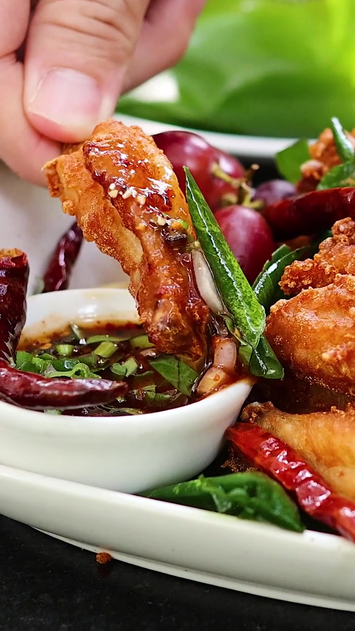 Una mano intinge un pezzo di pollo fritto dorato in una salsa thai piccante.
