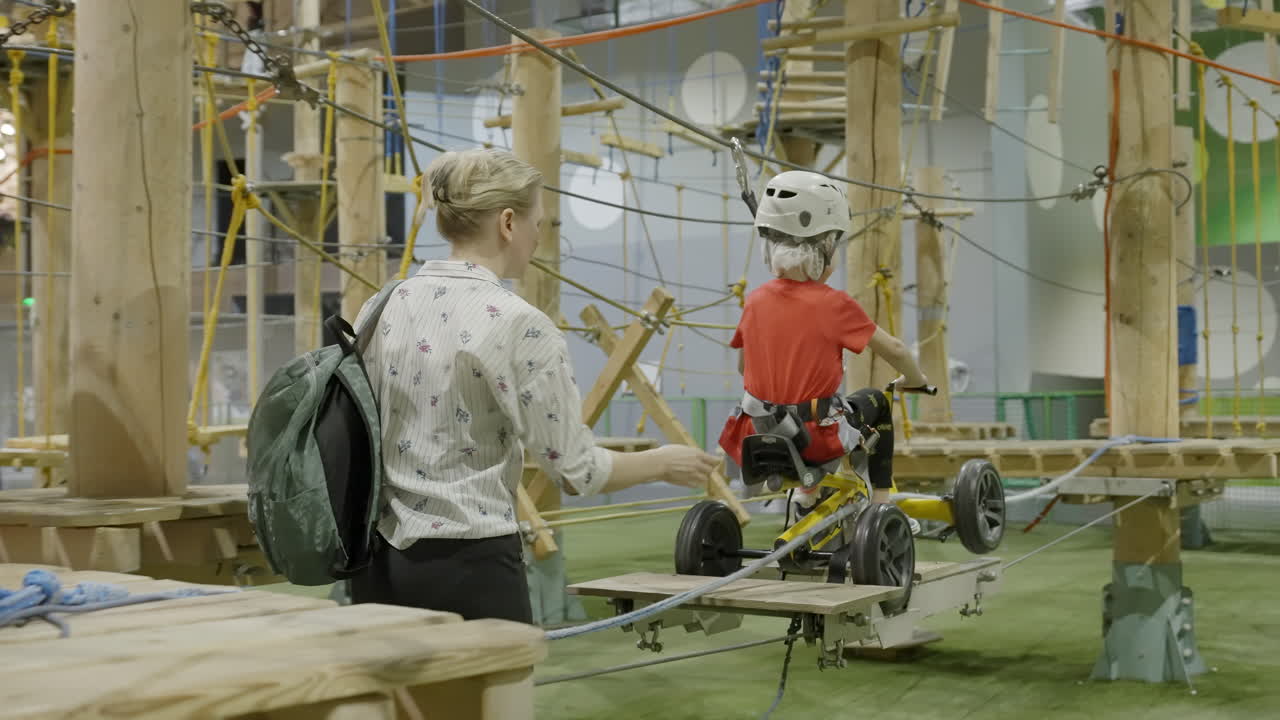 Woman assists child on an indoor adventure park rope course