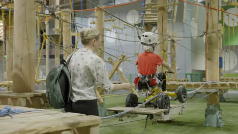 woman assists child on an indoor adventure park rope course