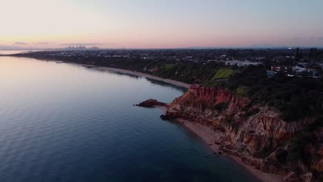 the striking red bluff cliffs stand tall, with the melbourne skyline visible in the distance, blending rugged nature with the urban landscape.