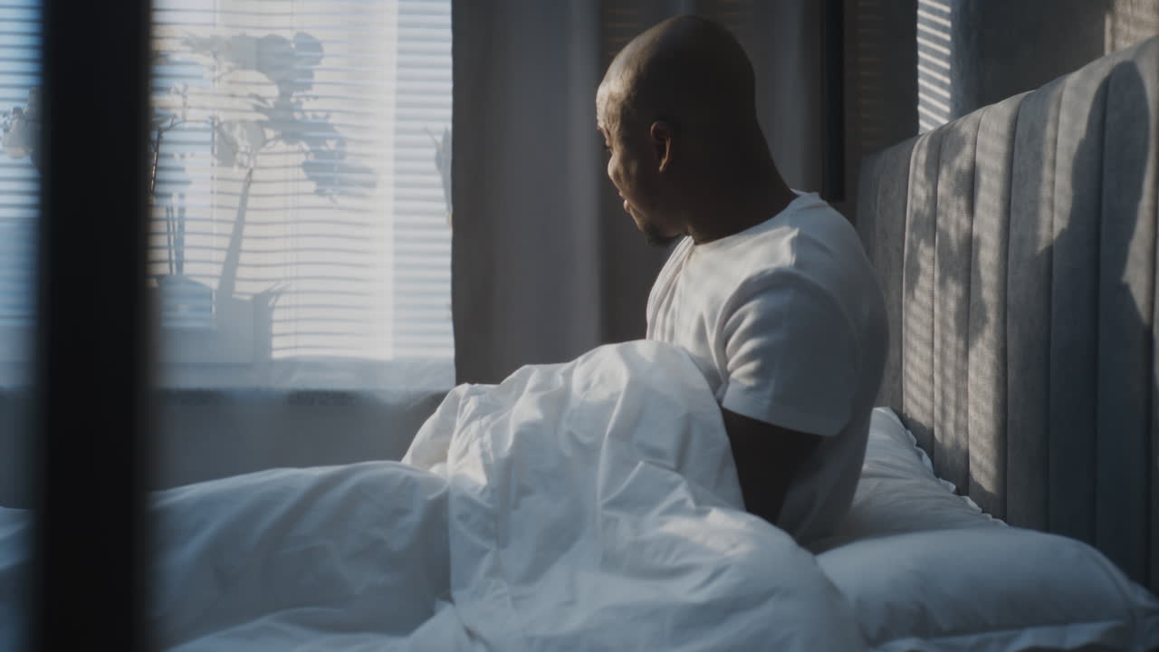 Adult Man Slowly Wakes Up Under Soft Blanket and Pulls Smartphone Out Under Pillows