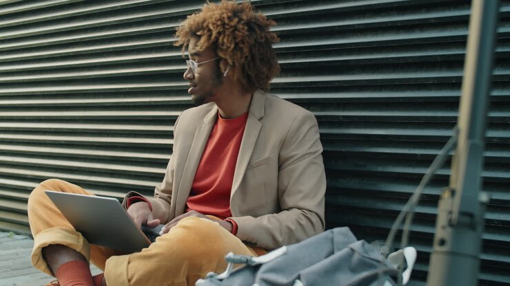 African American Man Sitting on Street and Video Calling on Laptop