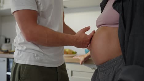 primer plano de un hombre feliz en una camiseta blanca acariciando el vientre de su esposa embarazada por la mañana en la cocina