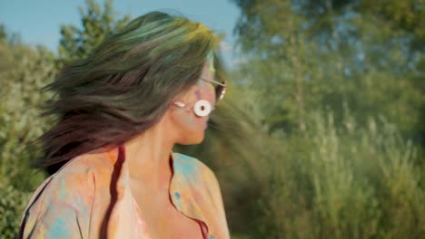 retrato en cámara lenta de una joven asiática alegre cubierta de pintura en polvo agitando la cabeza jugando con el cabello en el festival de holi
