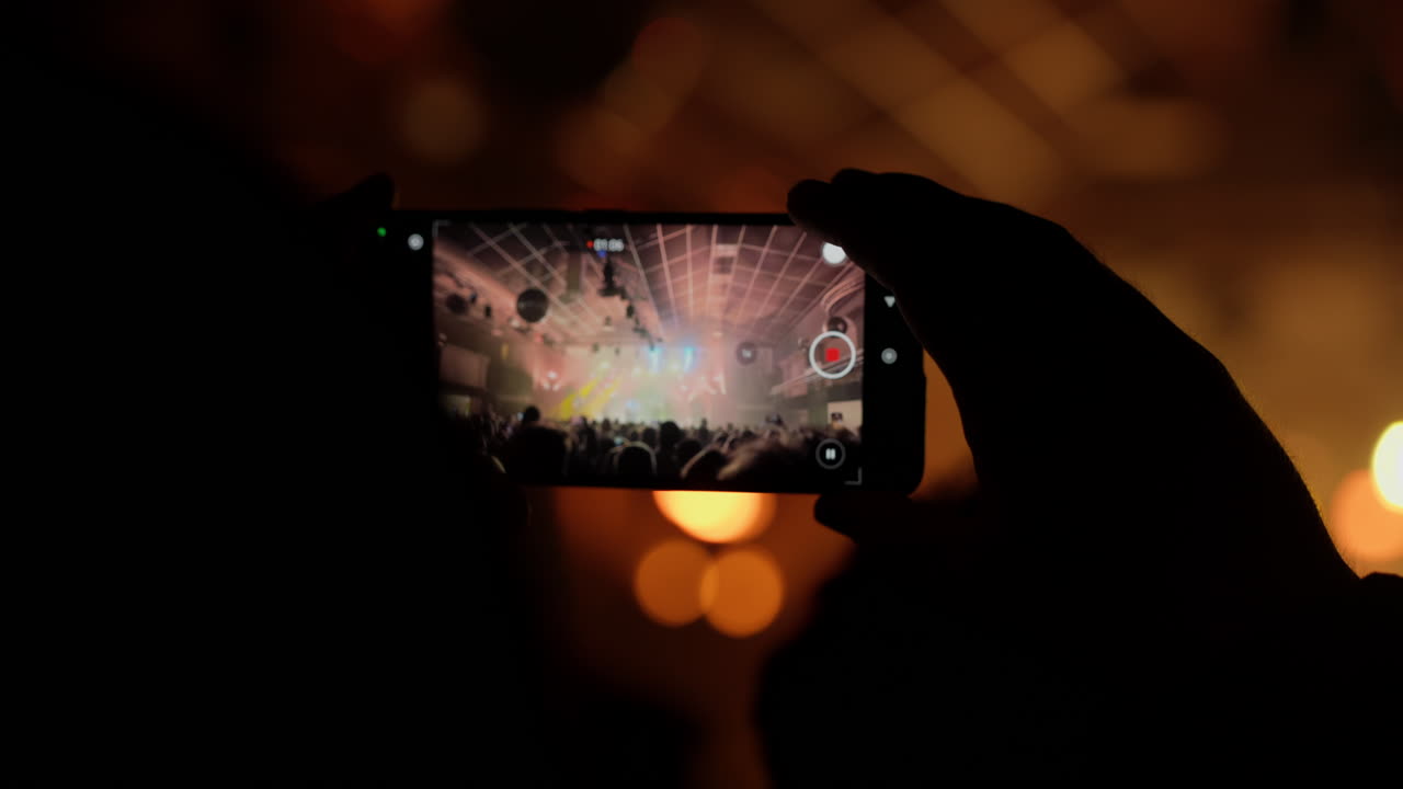 Persona che registra un concerto dal vivo con uno smartphone in un locale buio