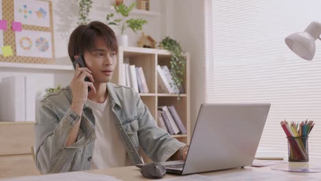 アジアのデザイナーがスマートフォンを使ってコミュニケーションをとる プロジェクトや書類に取り組む 家の机でラップトップで仕事をする