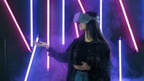 young woman playing, looks around and wonders how amazing  in the vr headset. virtual reality helmet on color lighting smoke background