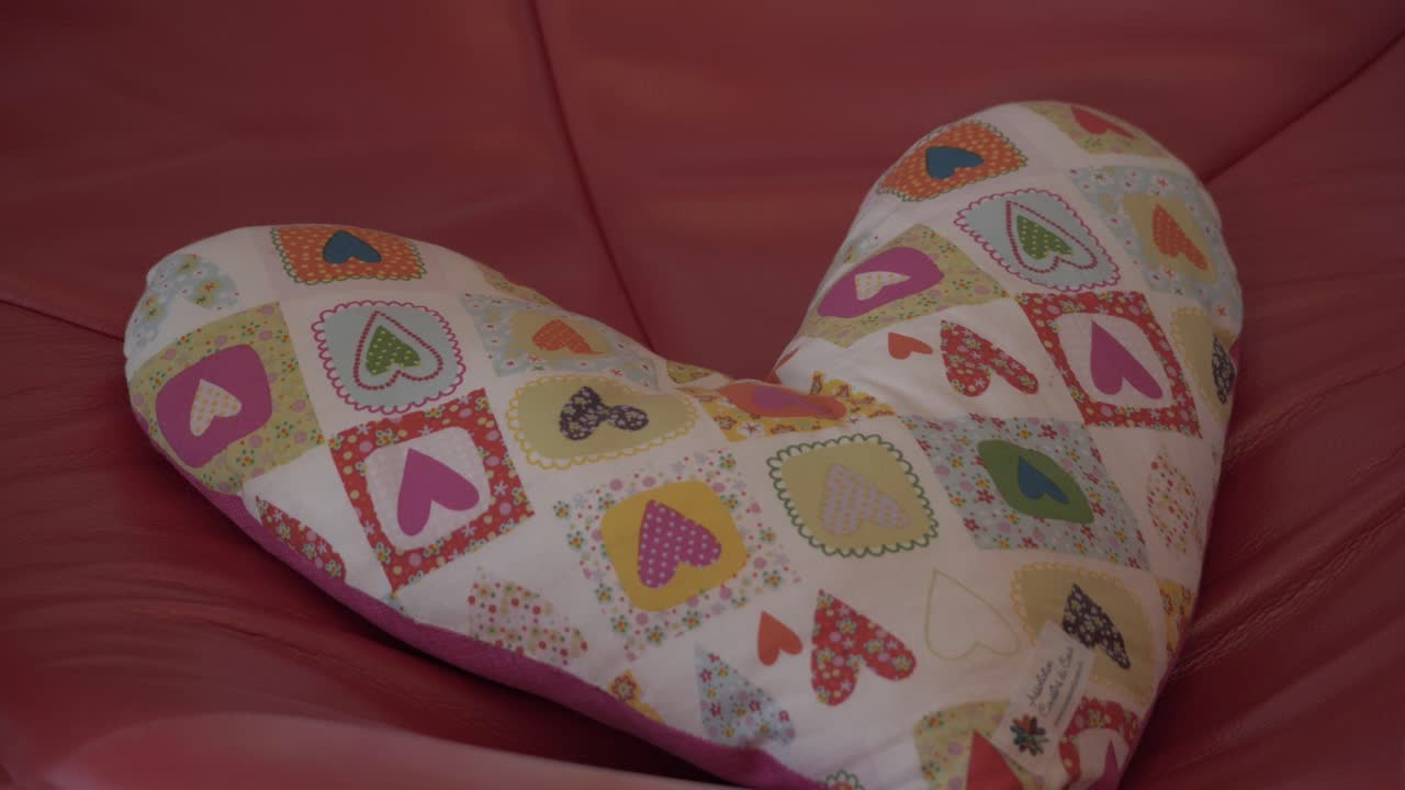 Handmade heart shaped cushion with diverse colorful patterns sitting on a bright pink surface. Close-up interior shot