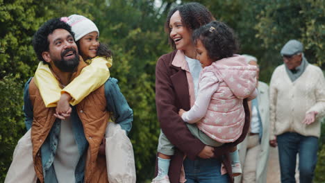 a family with two young daughters are walking in a park, smiling and laughing together.