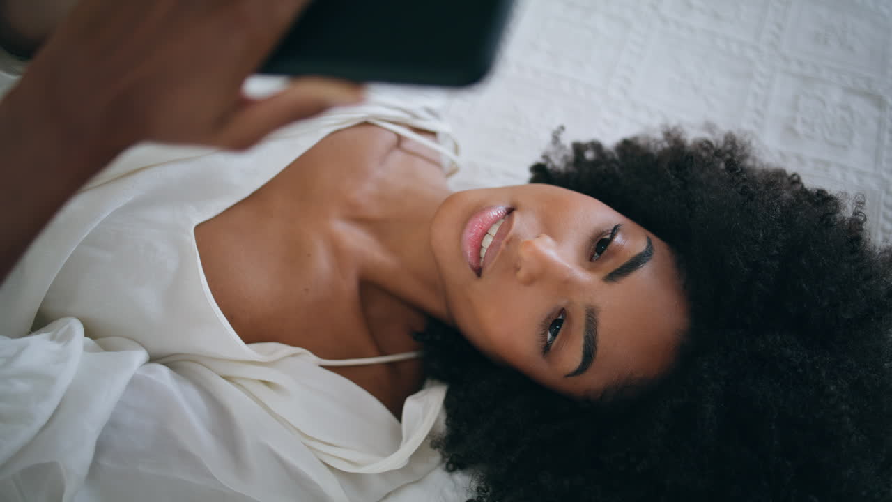 Peaceful girl read message bed alone. Calm african american lady laying bedroom