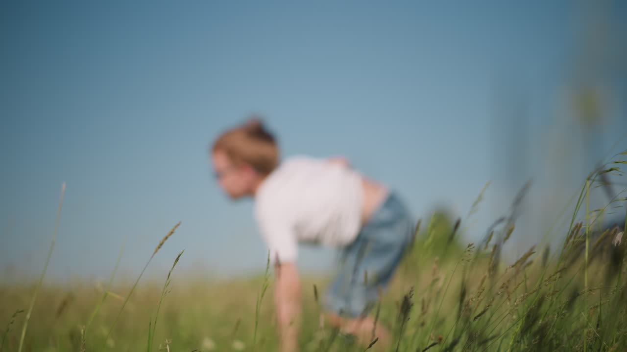 색 셔츠와 짧은 청바지를 입은 어린 소년이 빛이 넘치는 잔디에서 반복하는 모습을 포착합니다. 은 파란 하늘에 대한 역동적인 움직임은 자연에서 어린 시절의 놀이의 에너지와 기을 보여줍니다.