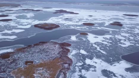 aerial view of frozen lake liepaja during the winter, blue ice with cracks, dry yellowed reed islands, overcast winter day, wide drone shot moving forward, camera tilt down