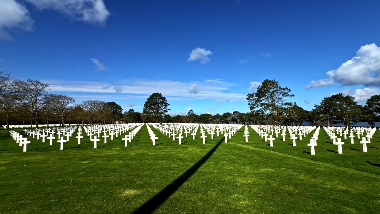 Infinite file di croci bianche segnano le tombe al Cimitero della Normandia, incorniciate da un cielo azzurro brillante. Ideale per documentari storici o tributi commemorativi.