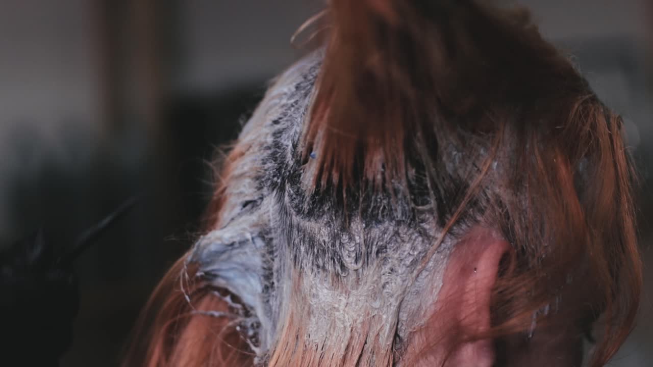 peluquero tiñendo el cabello de una mujer joven en una peluquería profesional