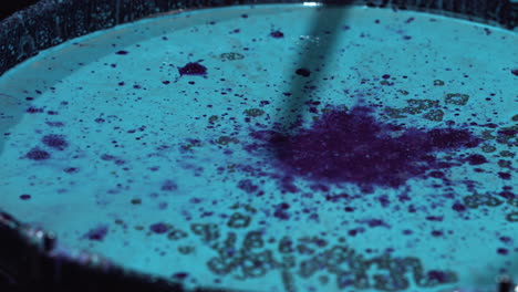 Playing-a-drum-that-is-filled-with-blue-and-purple-paint-that-splatters-when-the-drumsticks-hit