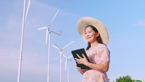 亞洲年輕女子在田野使用數碼平板電腦,背景是風力發電輪機