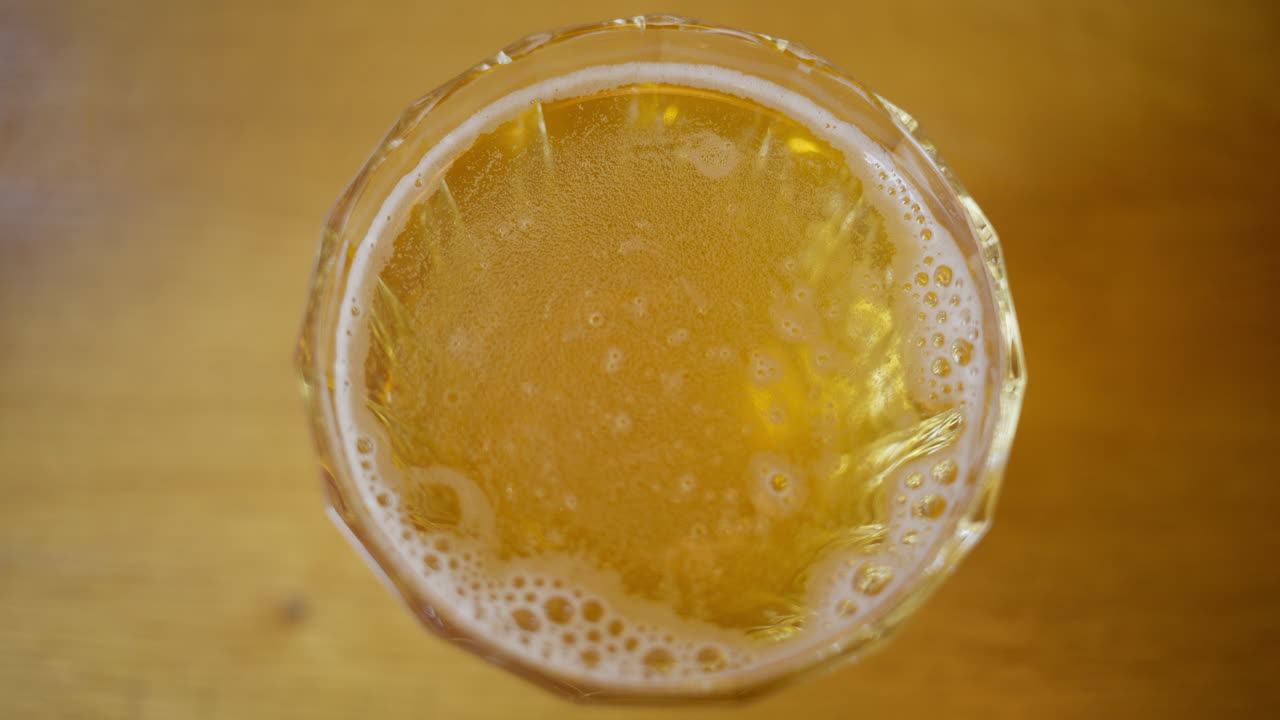 Vista dall'alto di un bicchiere di birra lager chiara appena versata con schiuma su un tavolo di legno.