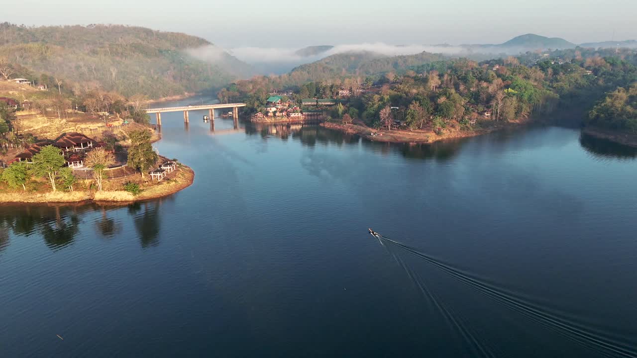 drone avanzando sobre el lago khwae noi, revelando el puente songkalia en el fondo, en songklaburi, tailandia