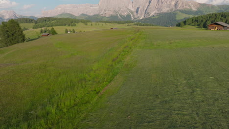 slow drone reveal shot of alpe di siusi during sunset, featuring peaceful mountain huts, vibrant grasslands and dolomite peaks