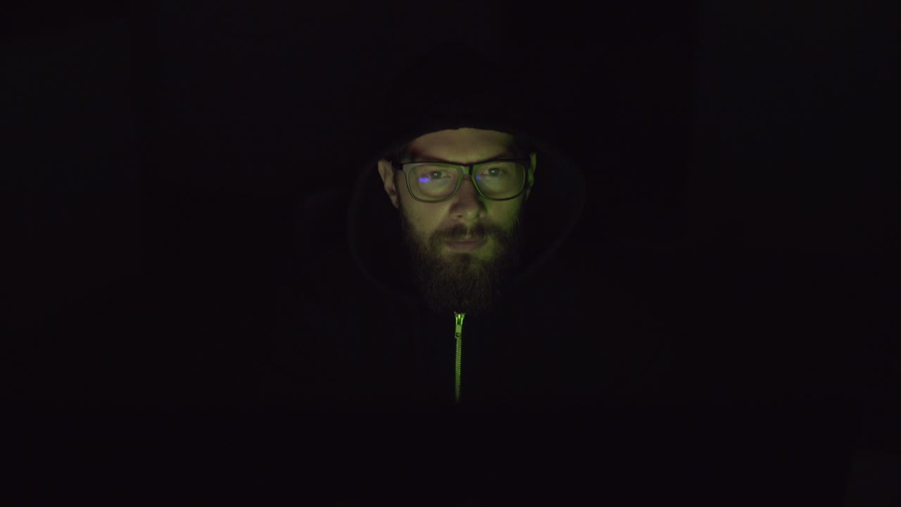 hacker con la cara descubierta está trabajando en la pc en el cuarto oscuro