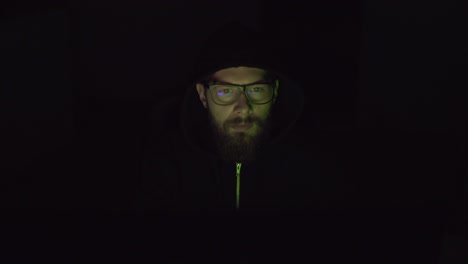 hacker with uncovered face is working on the pc in the dark room