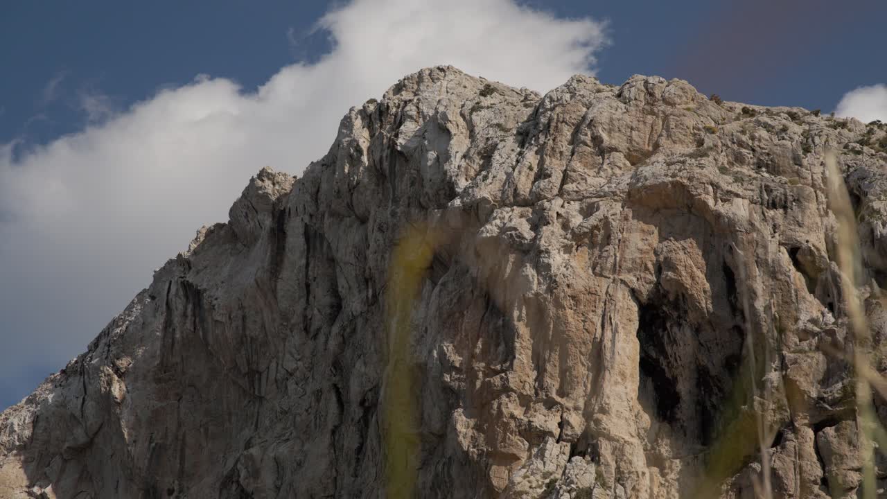 Steep rocky cliffs of Mallorca mountain range with sunlight and clouds passing above, telephoto