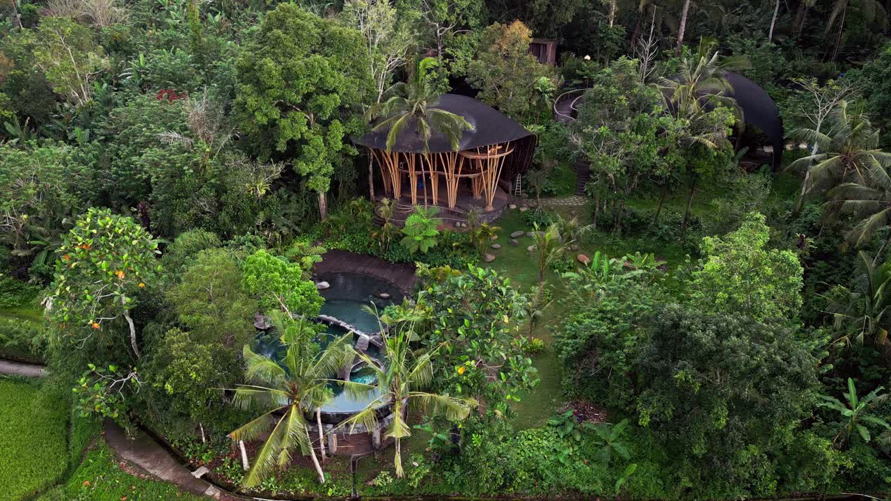 Drone footage of bamboo villas under construction surrounded by tropical gardens and lush green forest in Bali. A beautiful aerial view showing natural architecture blending perfectly with nature