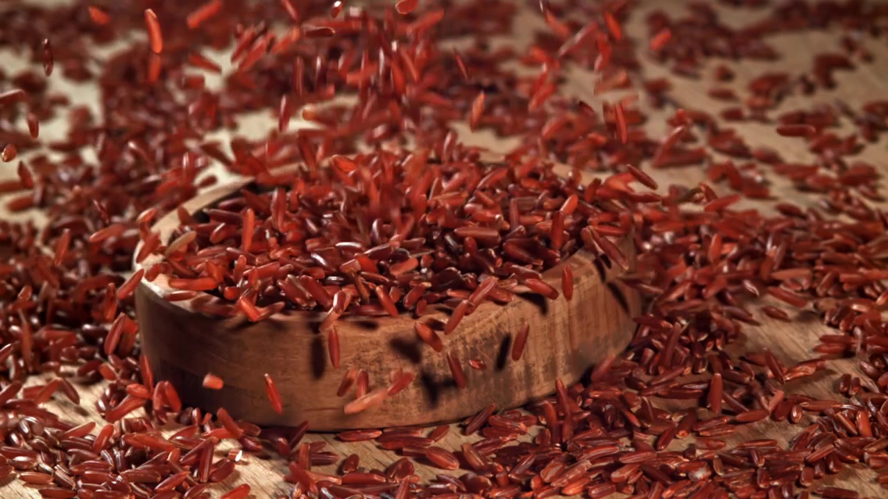 Rote Reiskörner fallen in Zeitlupe in eine Holzschale.