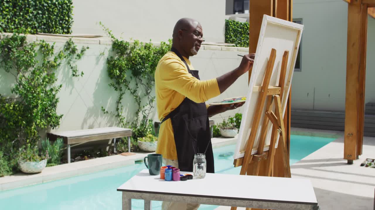 African american senior man standing on a terrace and painting