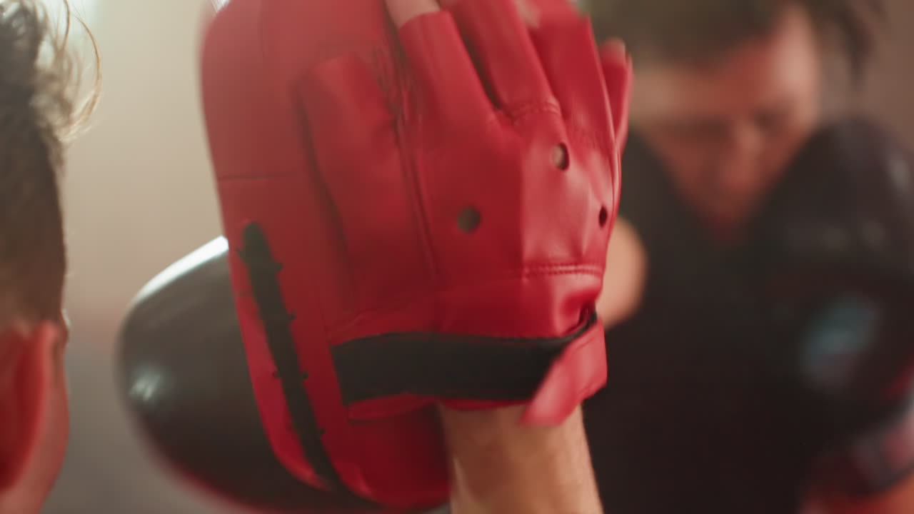 Closeup view of red boxing pad with trainer hand during boxer training session, capturing focus on equipment, leather surface, finger grip, and intensity of combat sports practice inside gym environment