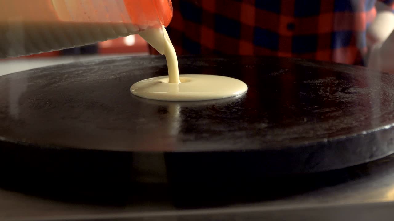 요리사는 뜨거운 스토브에 액체 팬케이크 반죽을 부어