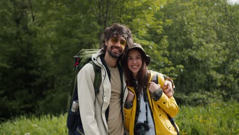 portrait of a pair of brunette guy brunette girl in special clothes for hiking stand looking at the camera and posing against the backdrop of a green forest