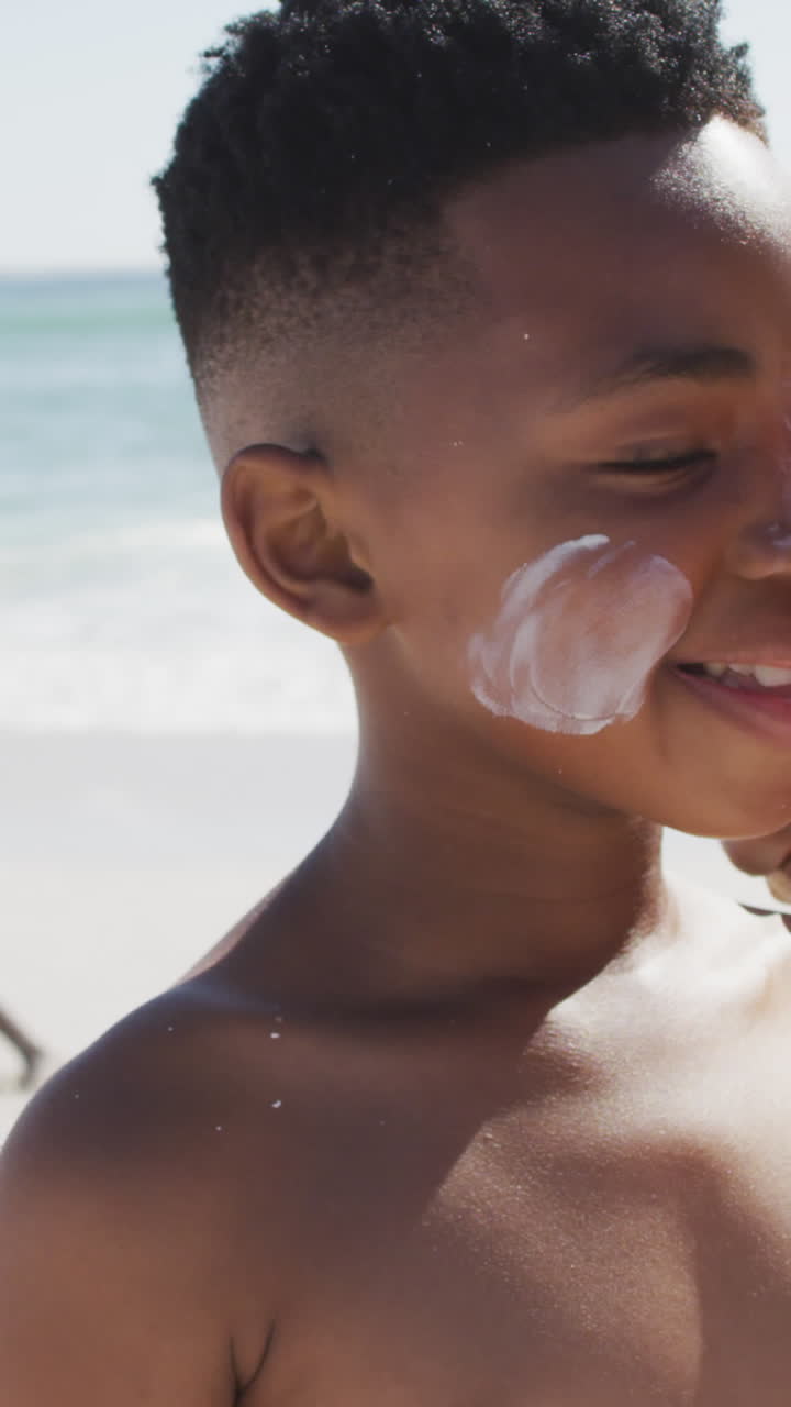 familia afroamericana sonriente usando crema solar en una playa soleada