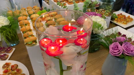 table with a variety of appetizers and tapas decorated with flowers and a jug with floating candles and an orchid submerged in the water