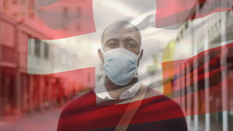 animation of flag of switzerland waving over man wearing face mask during covid 19 pandemic