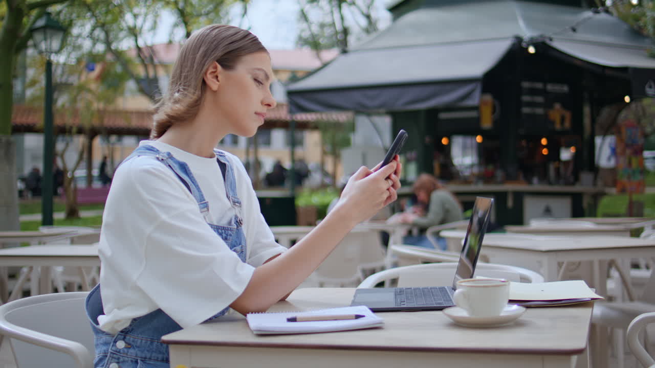 Relaxed woman checking cellphone message sitting street cafe with laptop closeup
