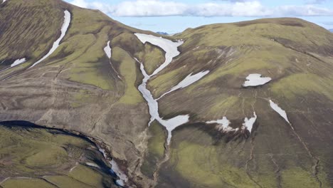 smooth aerial close-up focus on a green mountain with patches of snow in landmannalaugar, iceland