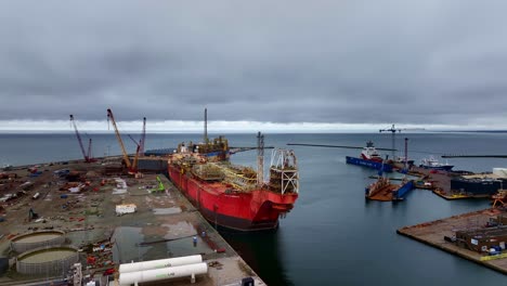 drone footage of a red tanker docked at the quay on a misty, overcast day. the drone approaches slowly from afar, capturing the vessel and atmospheric maritime surroundings.