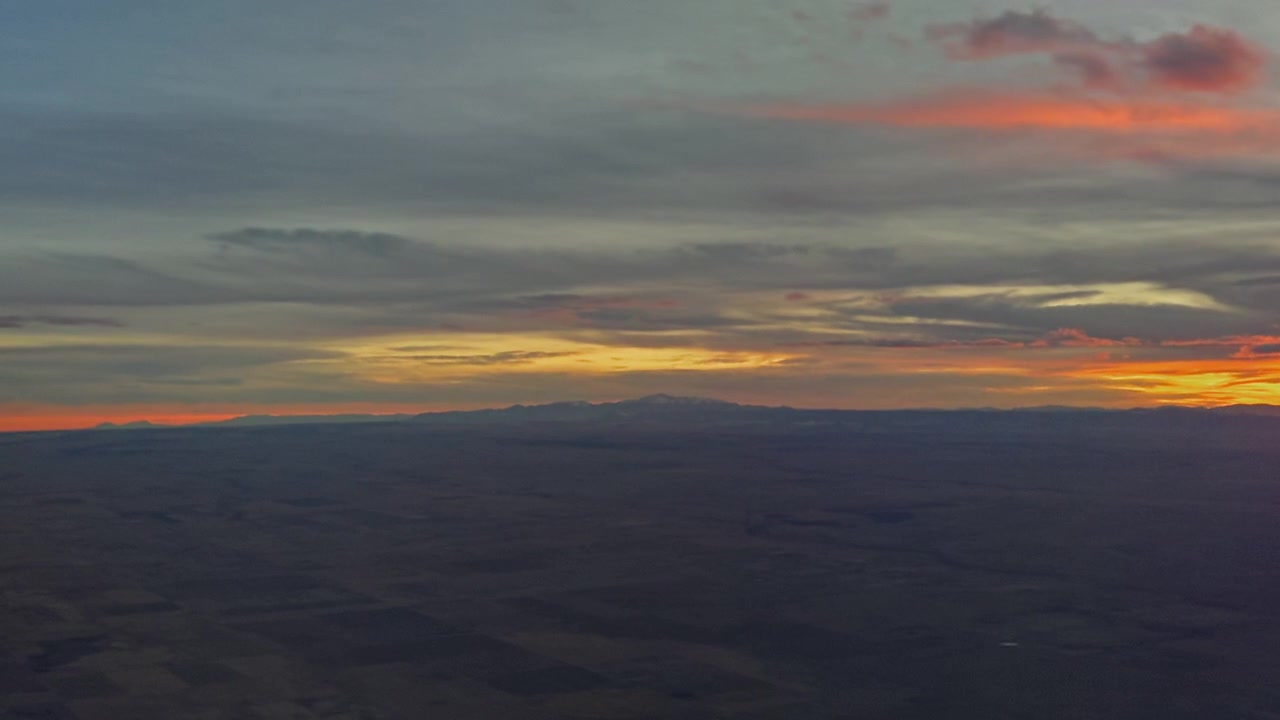 Colorful sunset clouds stretching across horizon above dark landscape below