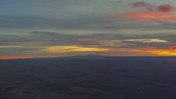 Colorful sunset clouds stretching across horizon above dark landscape below