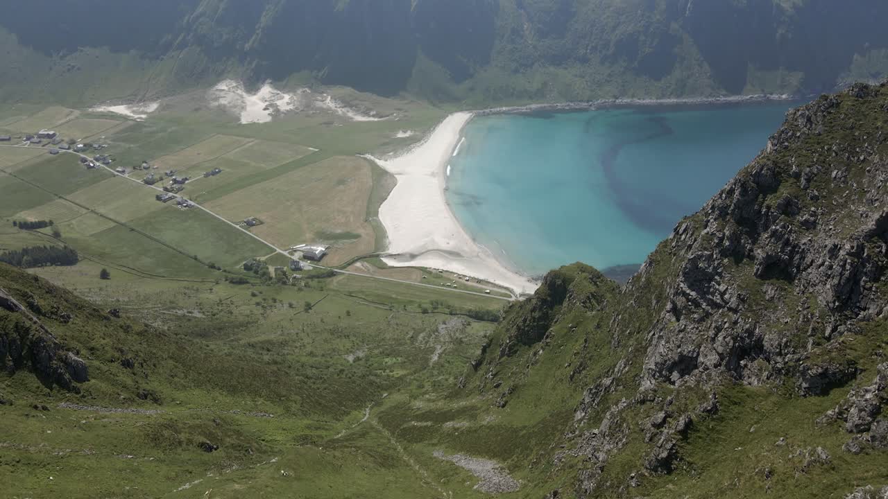 Ripresa aerea con inclinazione verso il basso di montagne verdi con spiaggia sabbiosa e baia turchese di Hoddevik in Norvegia