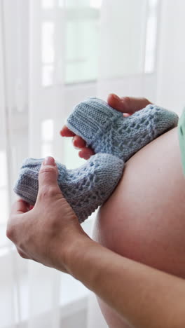 pregnant lady stands with her face to the window. mother plays with baby socks on her bag belly. the cat walks by on the window-sill behind the curtains. vertical video