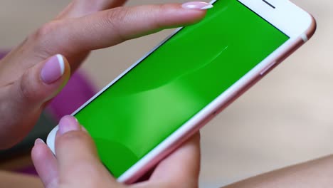 a woman is sitting in a cafe with a smartphone in her hands with a green screen mockup. the girl browses the internet, watches content, videos, blogs.