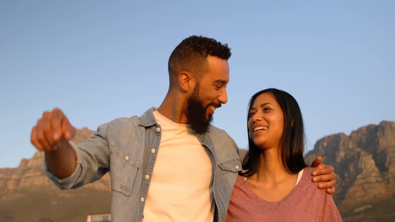 Joven pareja mestiza feliz de pie en la playa durante el atardecer 4k