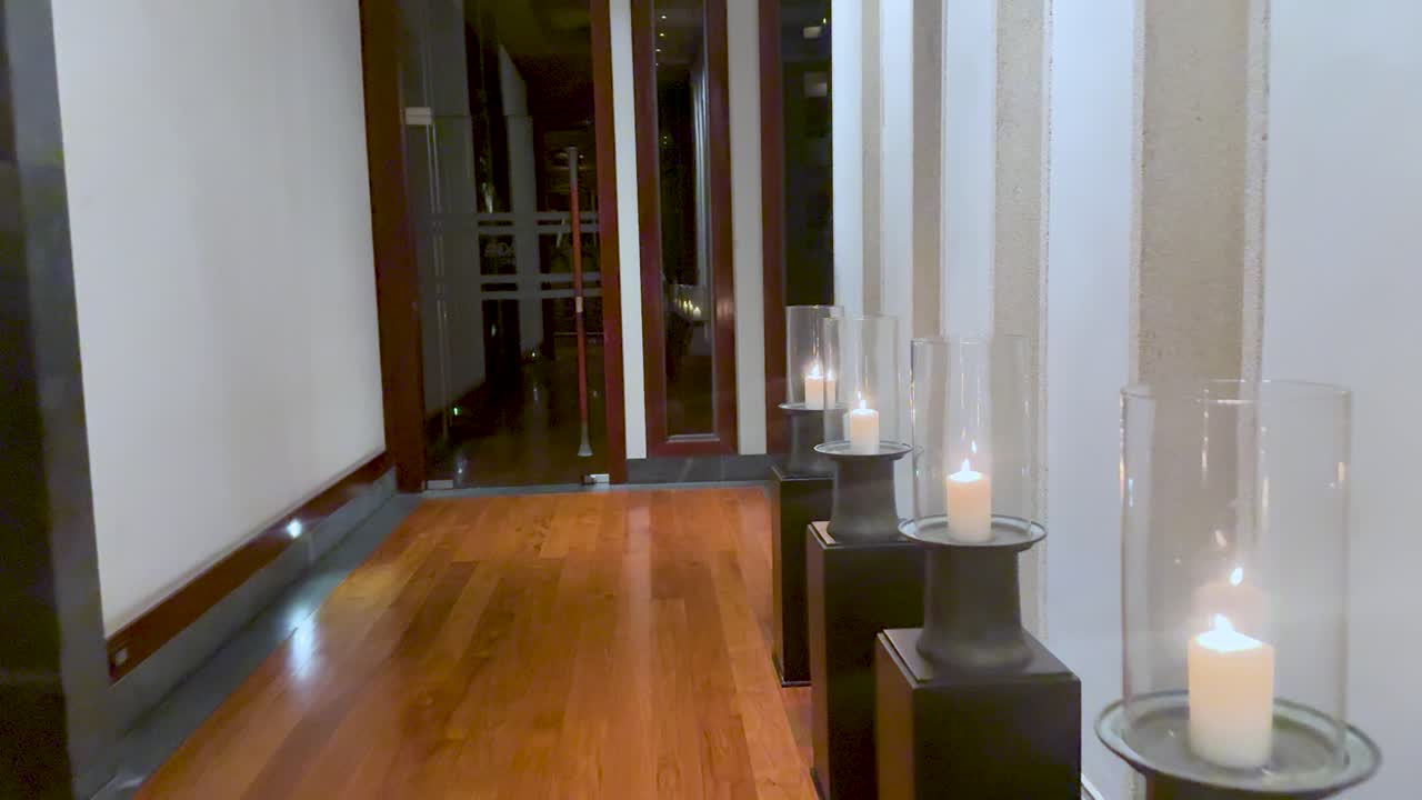 Un lento movimento di macchina cattura candele che brillano in lanterne di vetro lungo un corridoio di legno.