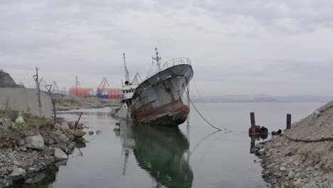 rusty grey half submerged shipwreck anchored near the shore on a cloudy overcast day