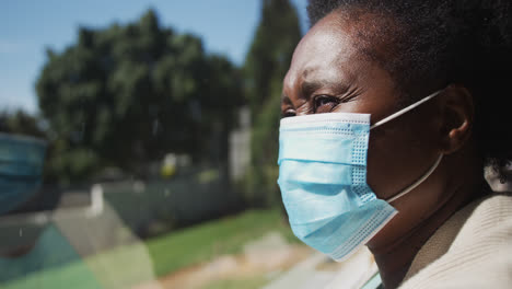 senior african american woman wearing face mask standing by window in slow motion