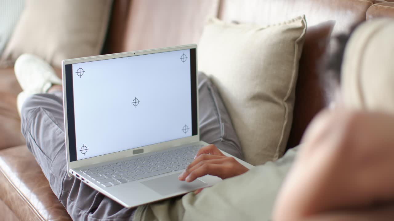 Uomo adulto sdraiato sul divano che reagisce al display con mirino del laptop, provando la mano destra sul trackpad.