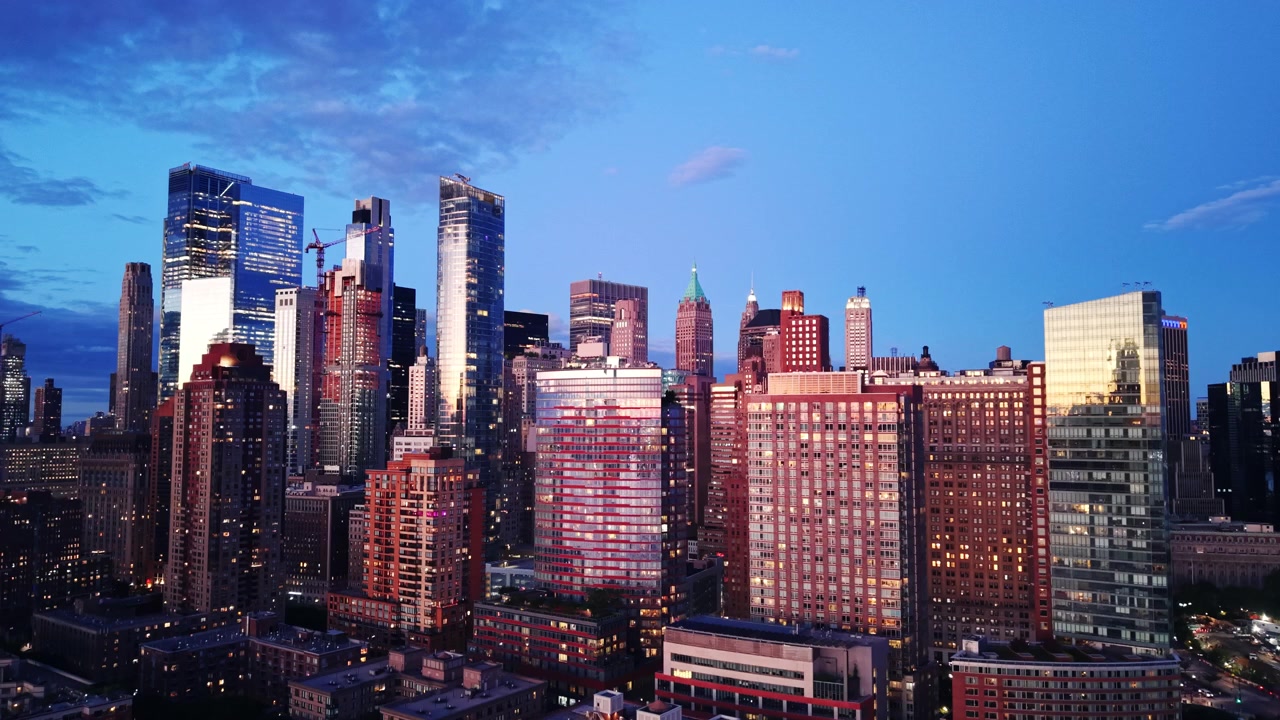 Torri urbane al crepuscolo, New York City. Prospettiva aerea di facciate di edifici in vetro che riflettono il cielo dell'ora blu, finestre illuminate e gru da costruzione sullo sfondo